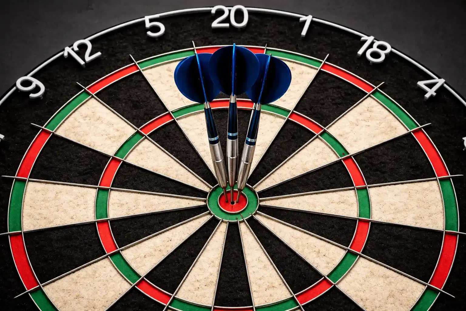 Drei Dartpfeile stecken dicht beieinander im Bullseye einer Dartscheibe